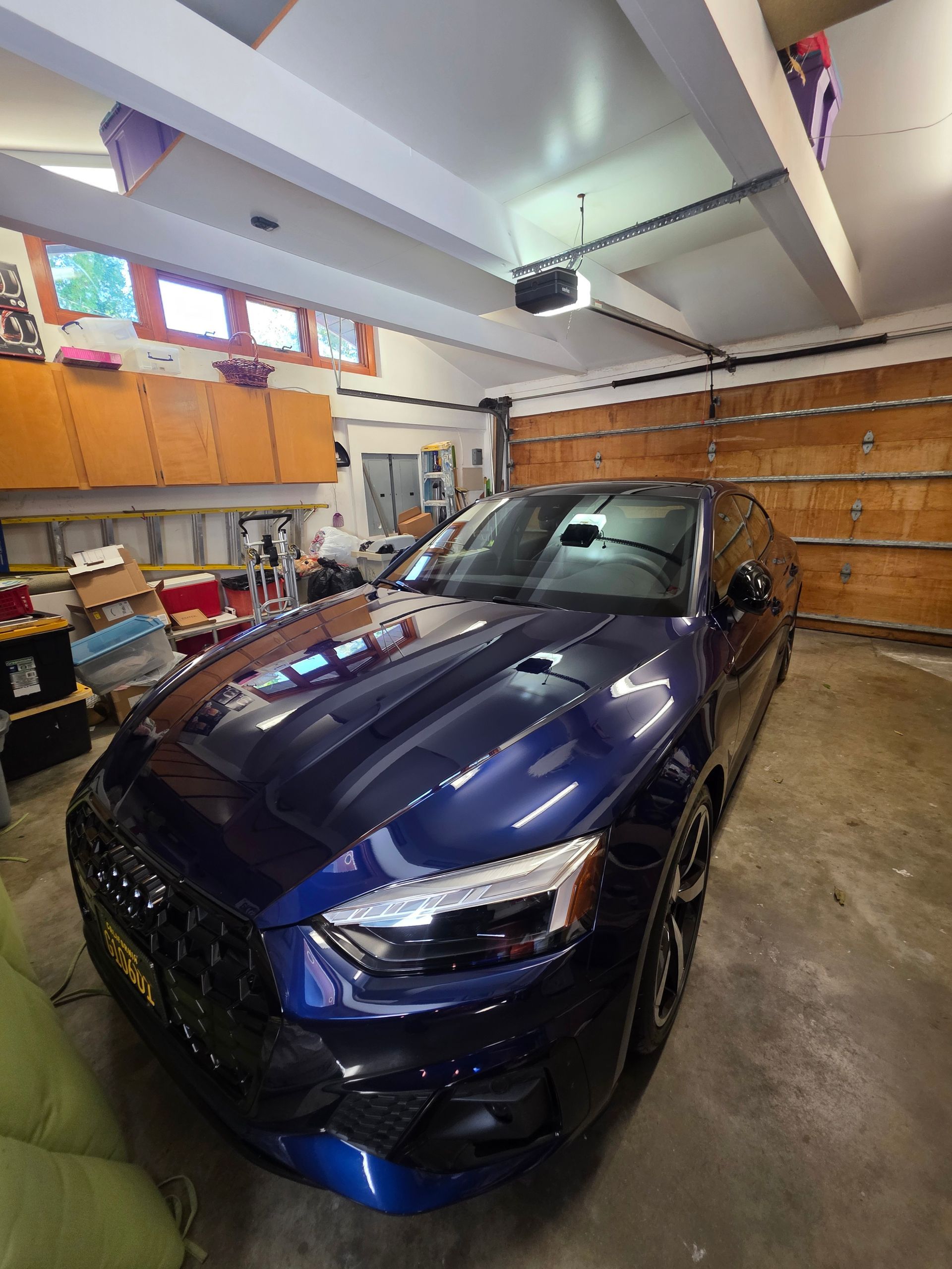 A dark blue sports sedan parked in a garage with orange cabinets and a wooden door.