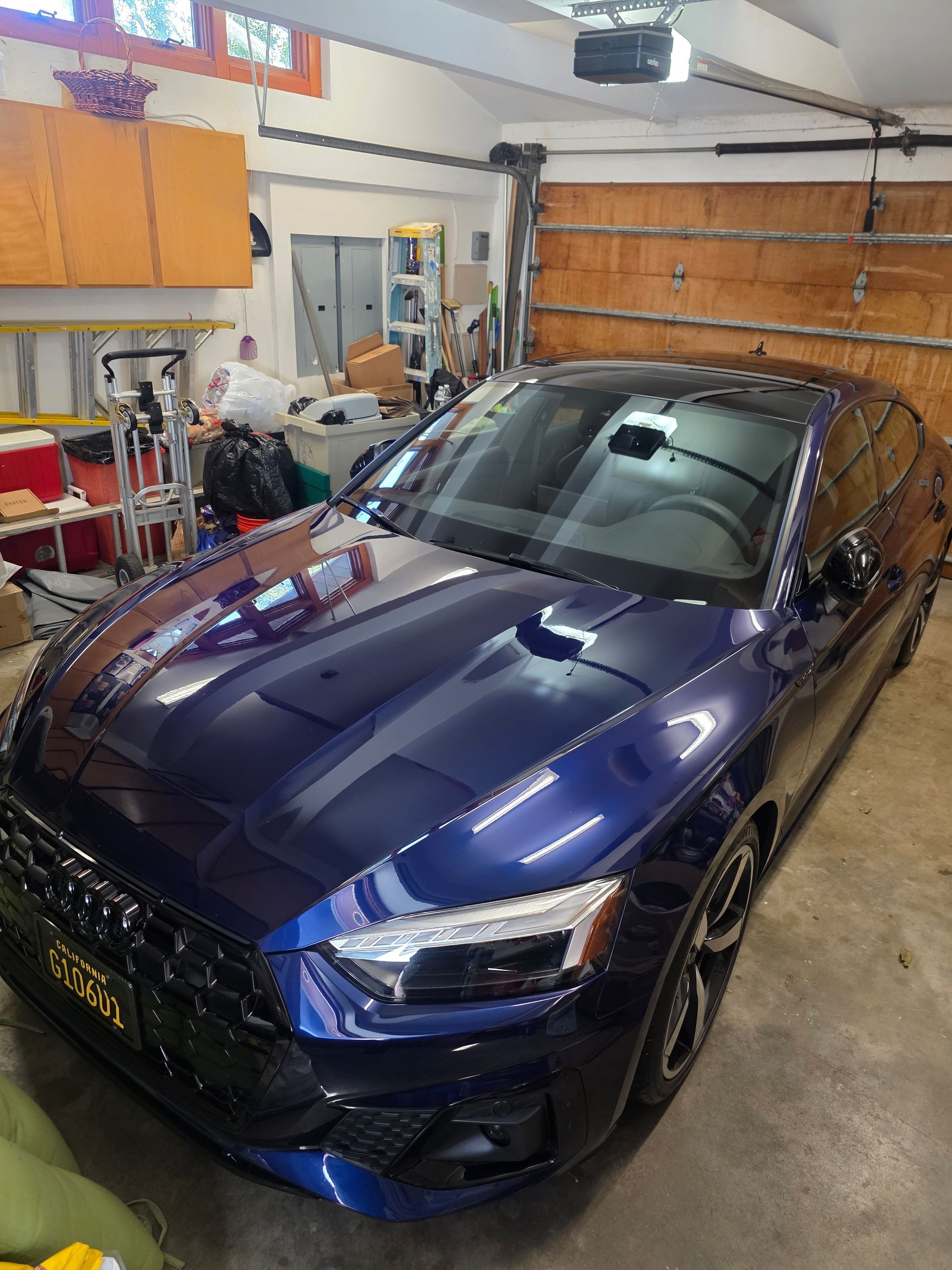 A deep blue Audi parked in a cluttered home garage with wooden cabinets and a brown panel garage door in the background.