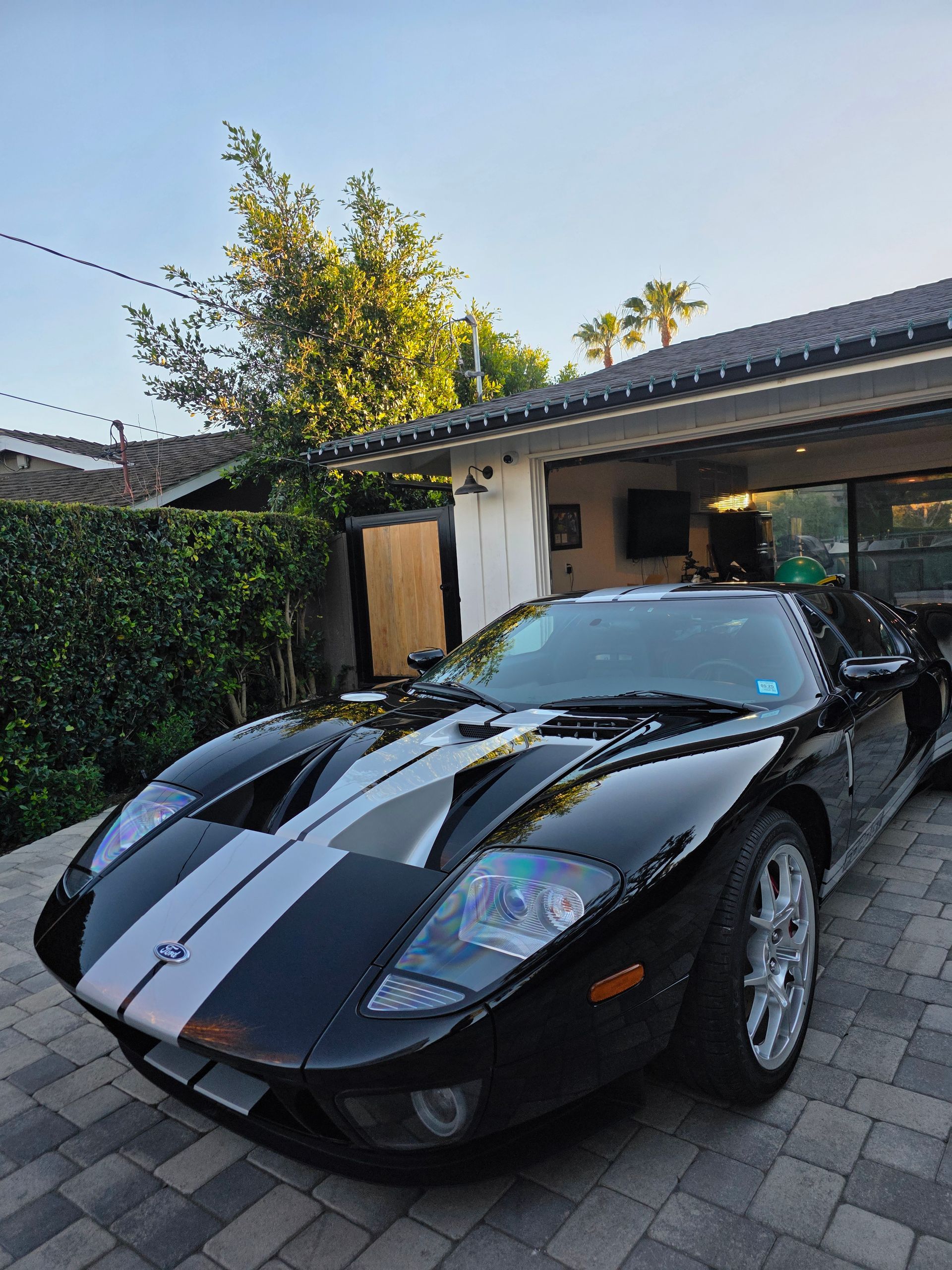 A black Ford GT supercar with dual silver racing stripes parked on a paved driveway in front of a house.