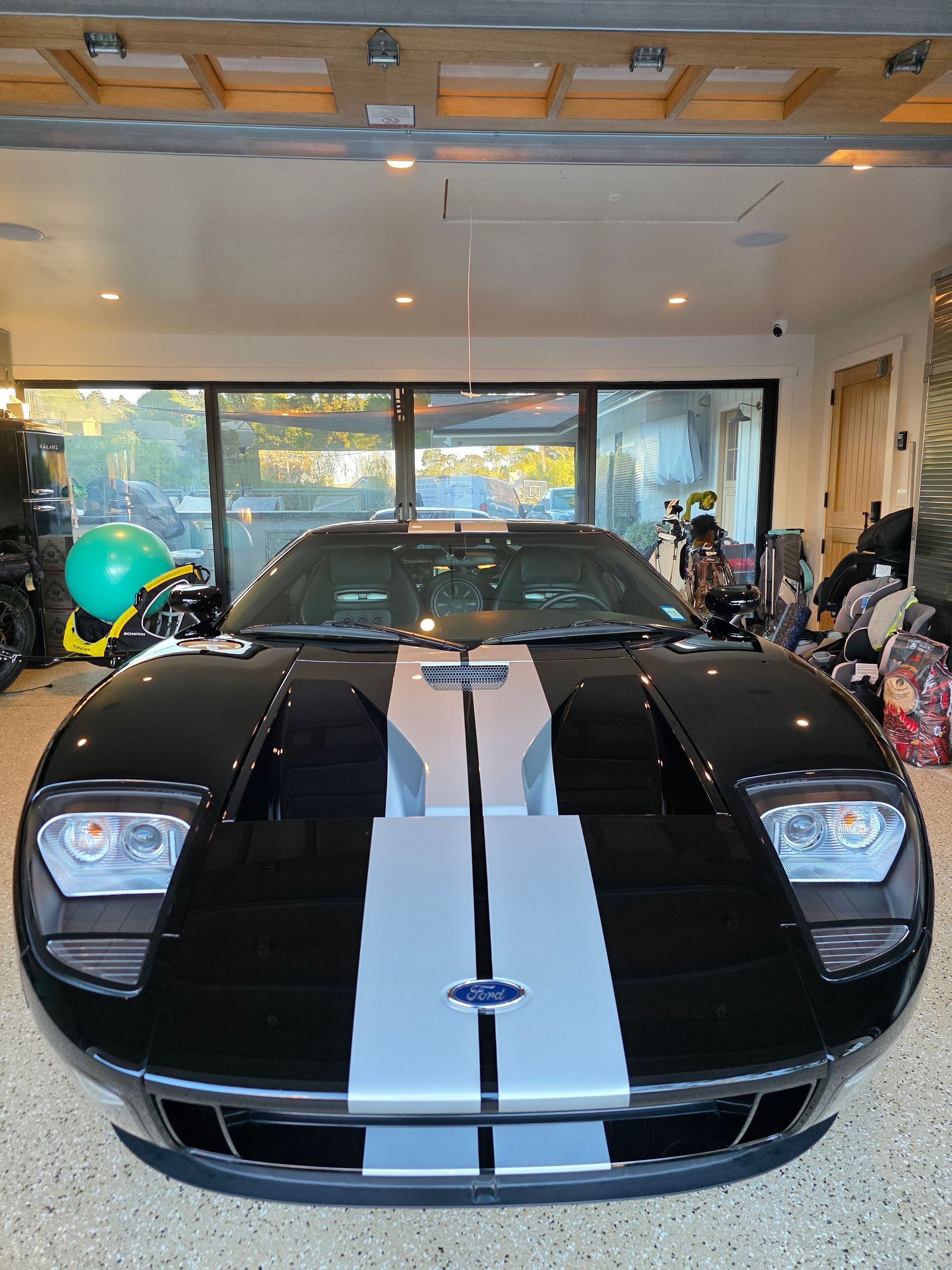 A black Ford GT supercar with silver racing stripes is parked in a well-lit residential garage.