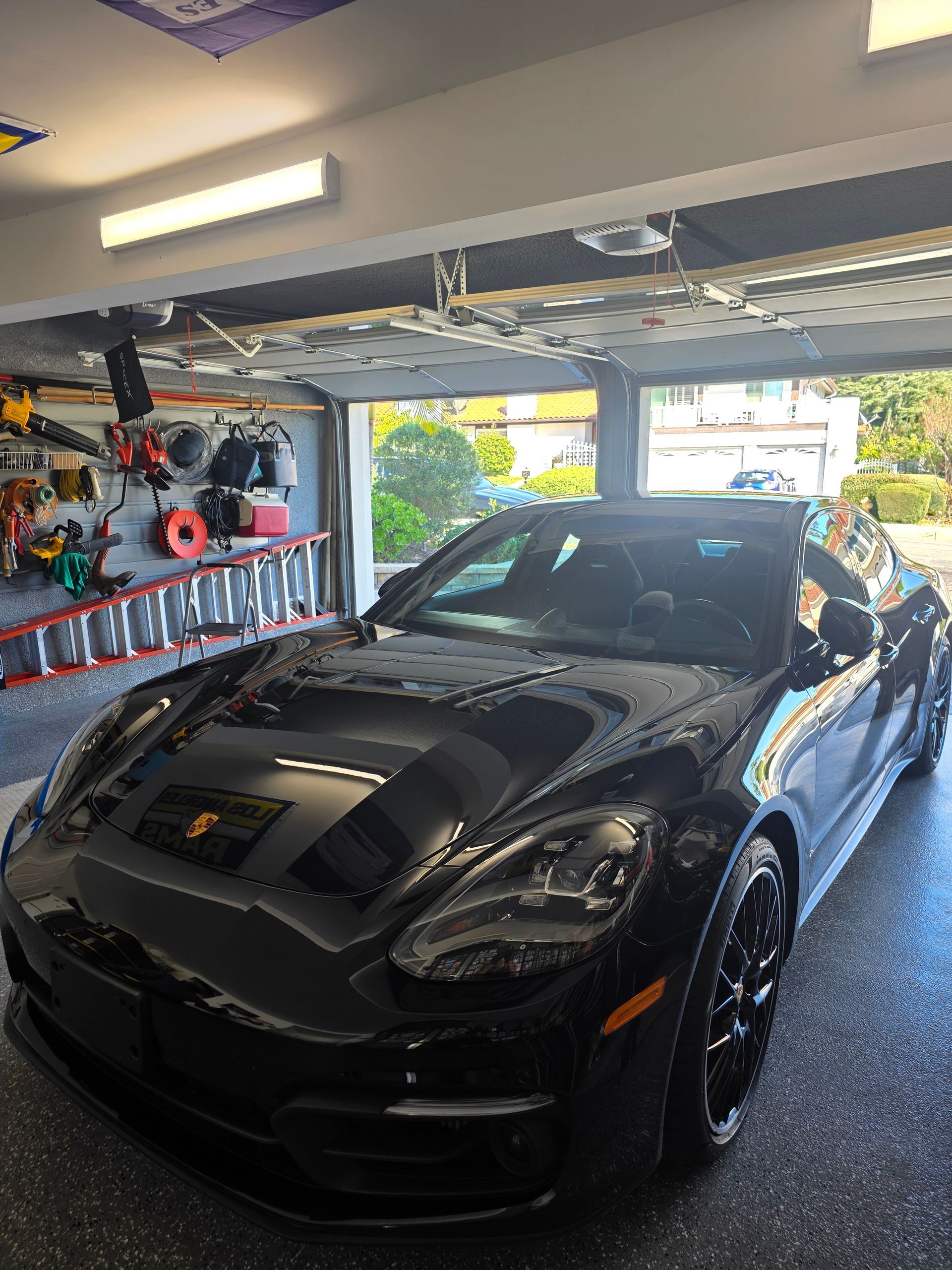 A shiny black Porsche parked inside a well-organized garage with tools and equipment hanging on the wall.
