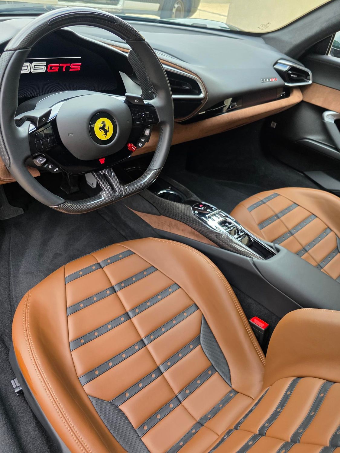 Ferrari sports car interior with tan leather seats, black dashboard, and steering wheel with yellow Ferrari logo