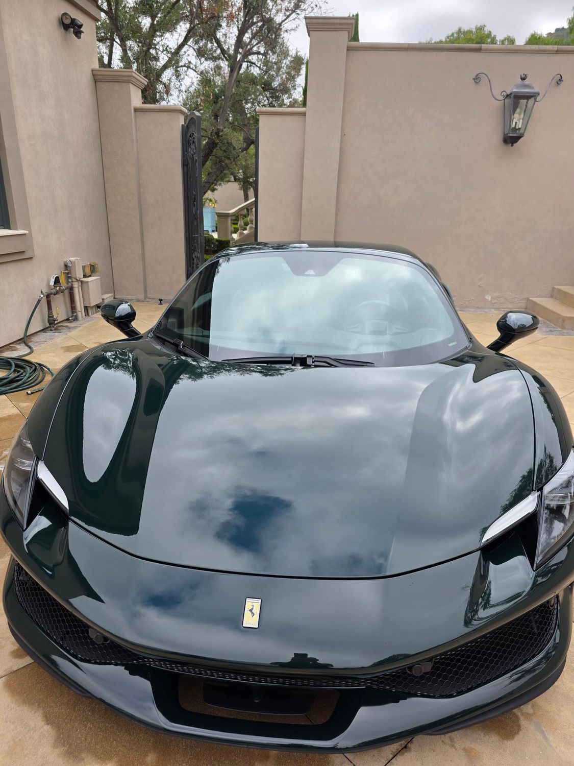 Black Ferrari sports car parked in a beige courtyard driveway, front view