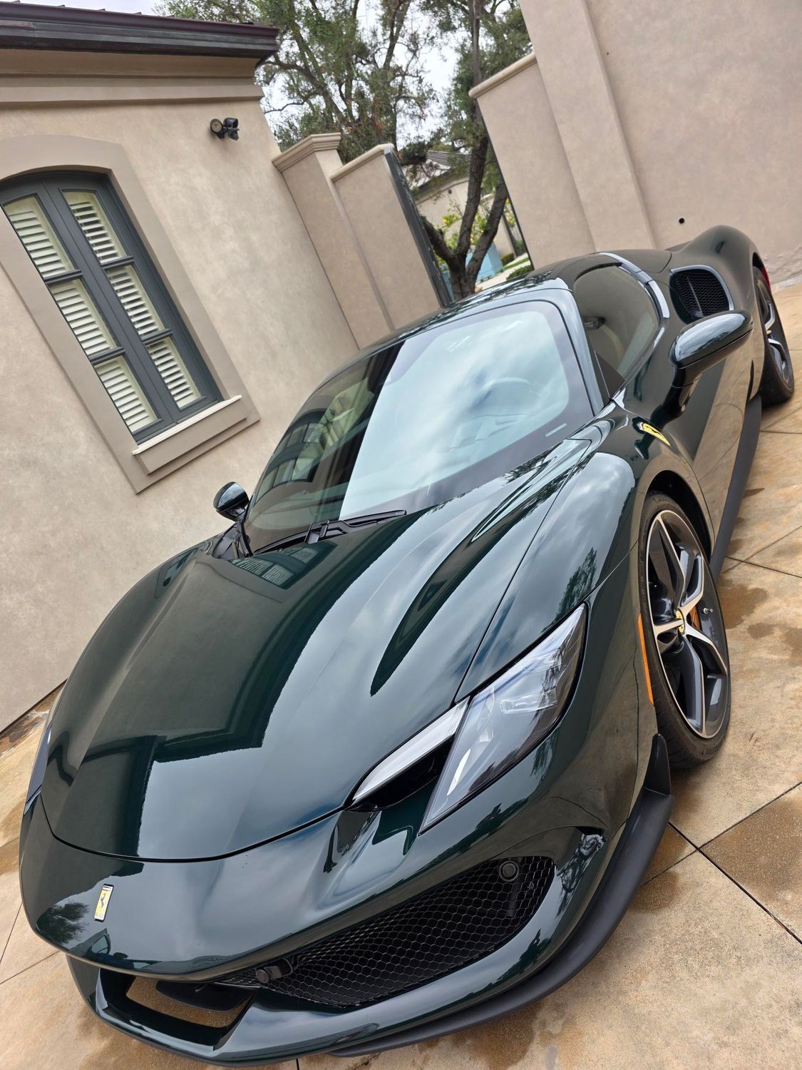 Black sports car parked in a driveway beside a beige house, angled front view.