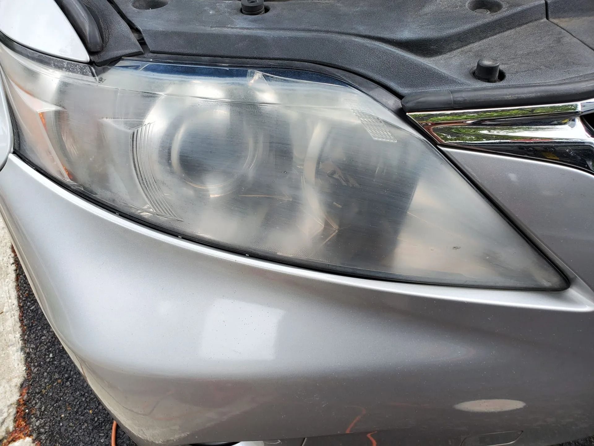 A closeup of a silver car's clouded, oxidized headlight lens in need of restoration.