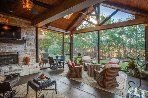 Screened-in porch with fireplace, seating, dining table, and view of trees.