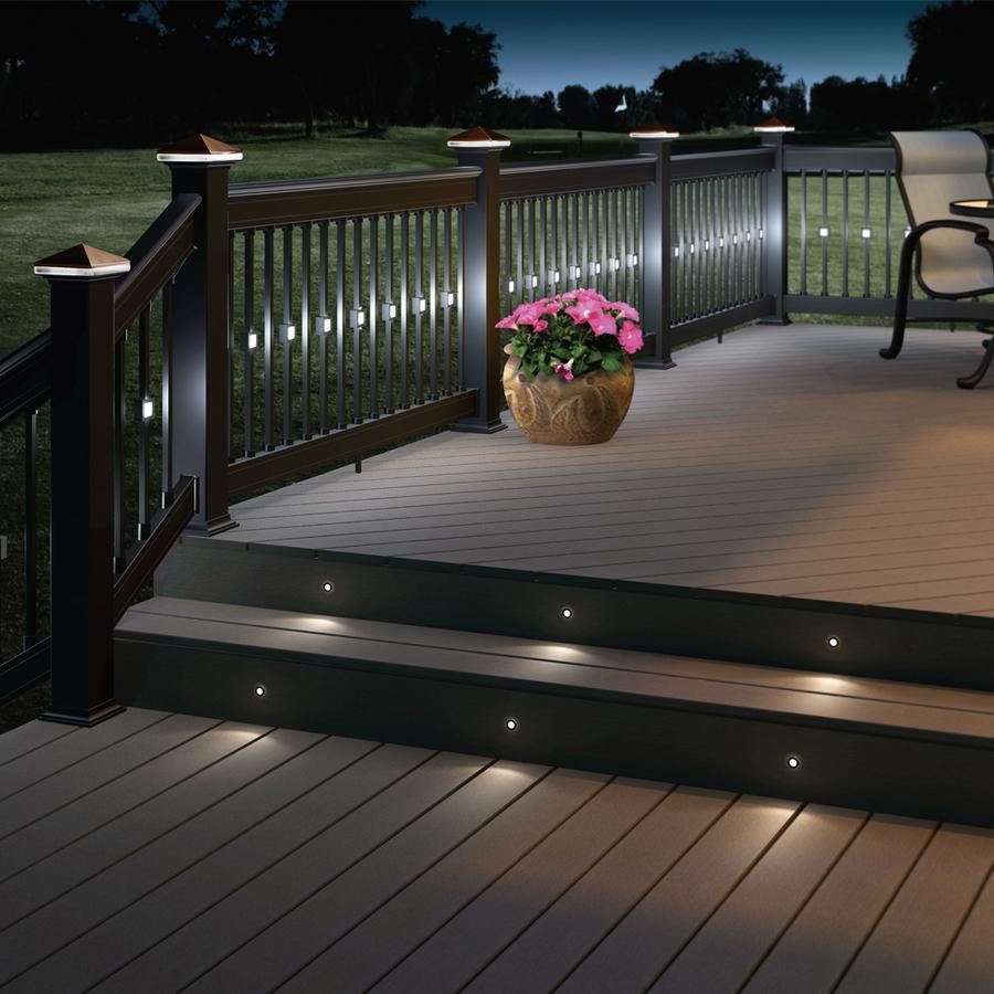 Lit deck with black railing and steps; flower pot on deck. Evening view.