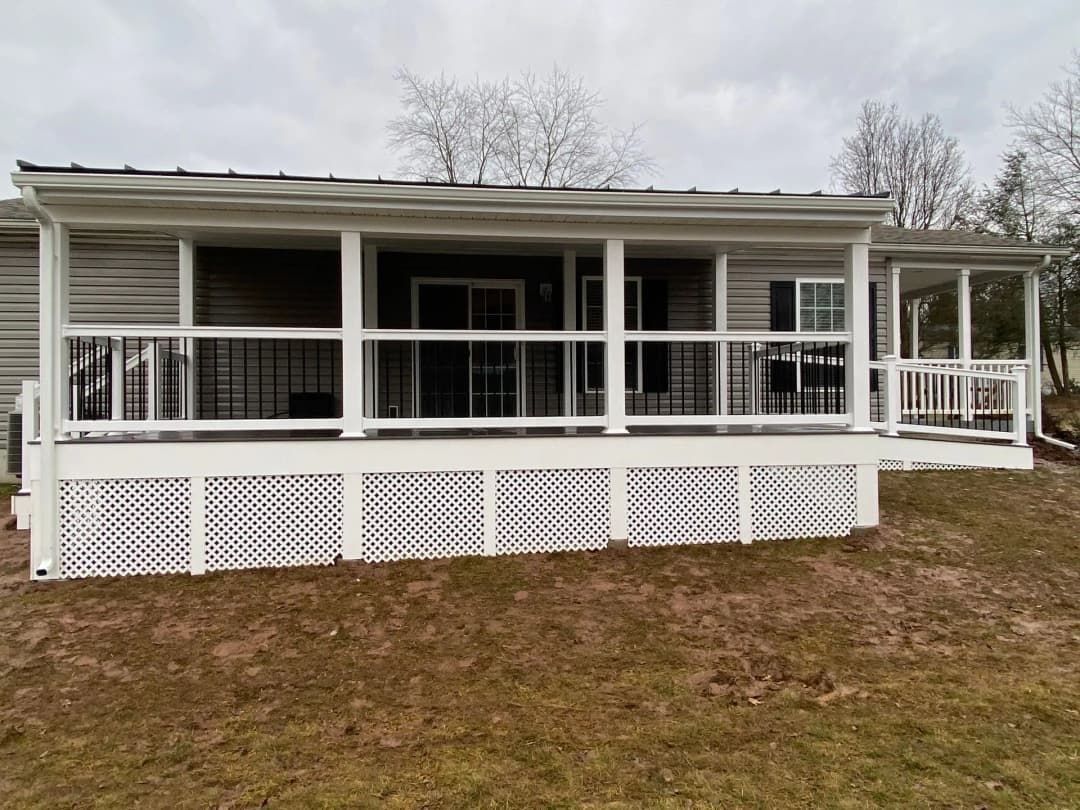 White covered deck with lattice skirting and railing, attached to a house with sliding glass doors.