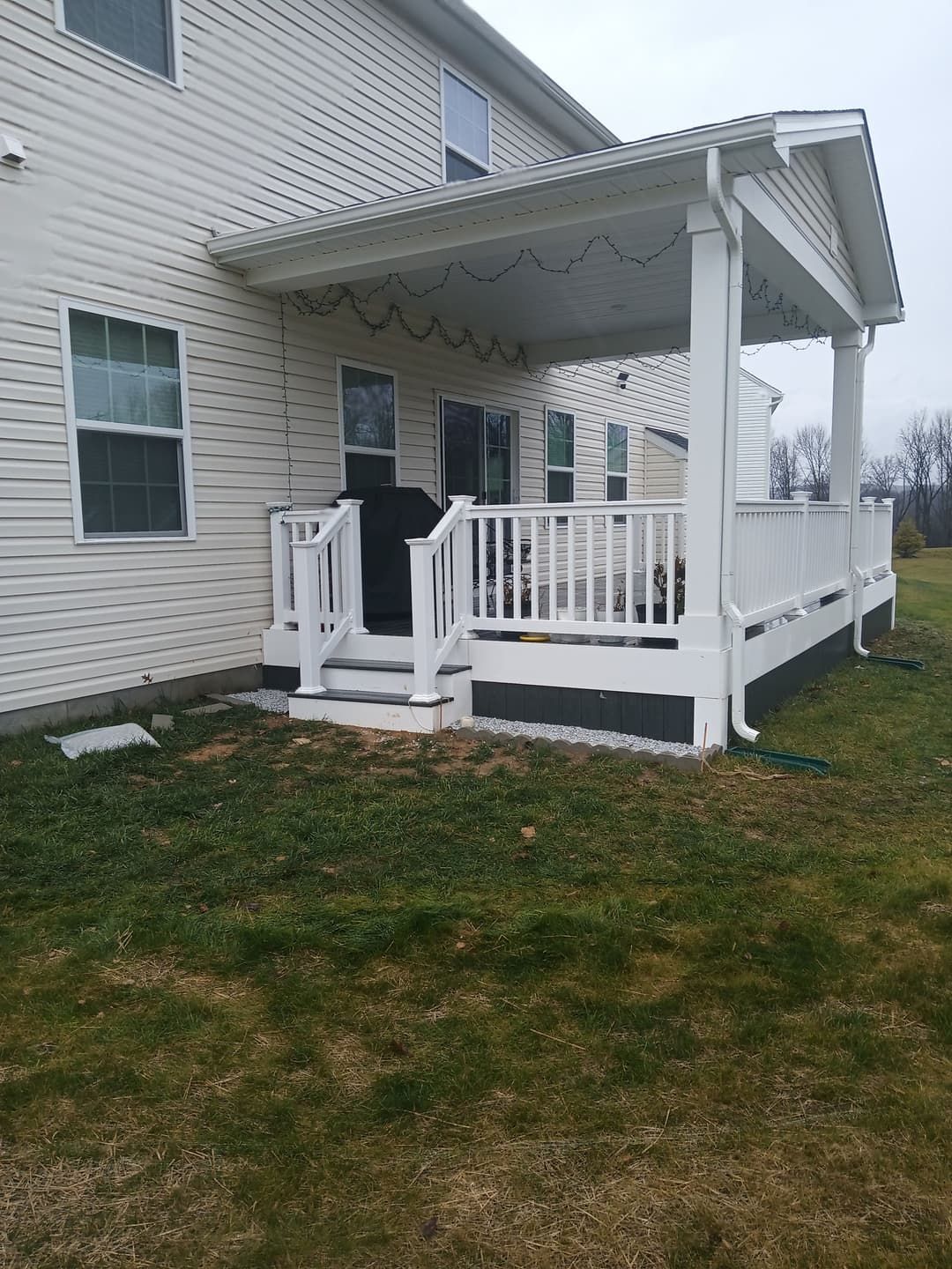 White covered porch attached to a two-story house with white siding and a grassy yard.