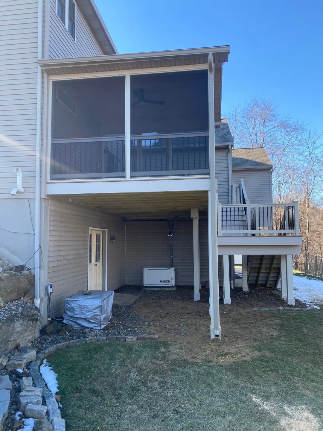 Two-story house with screened porch. Underneath, a generator, door, and patio area. Green grass and snow.