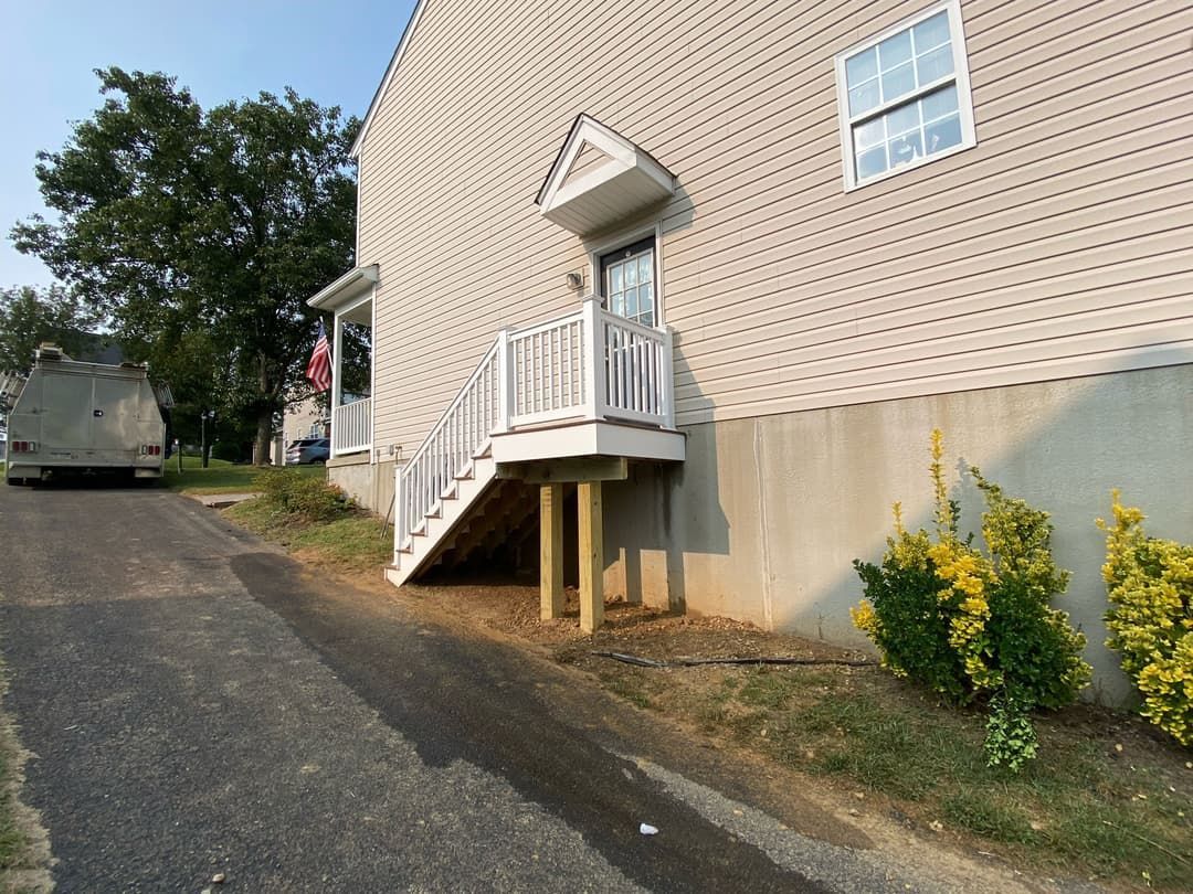 Side view of a house with a raised entrance platform and stairs; asphalt driveway.