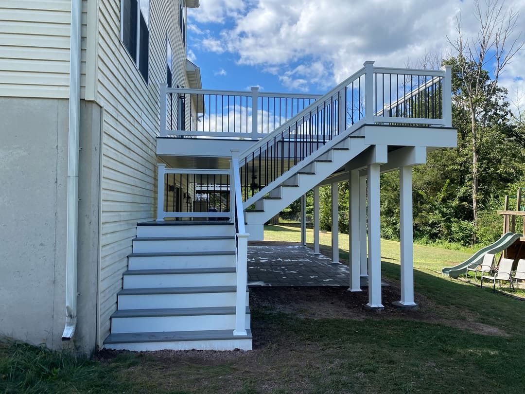 White deck with stairs, black railing, attached to a light-colored house. Green grass in the yard.