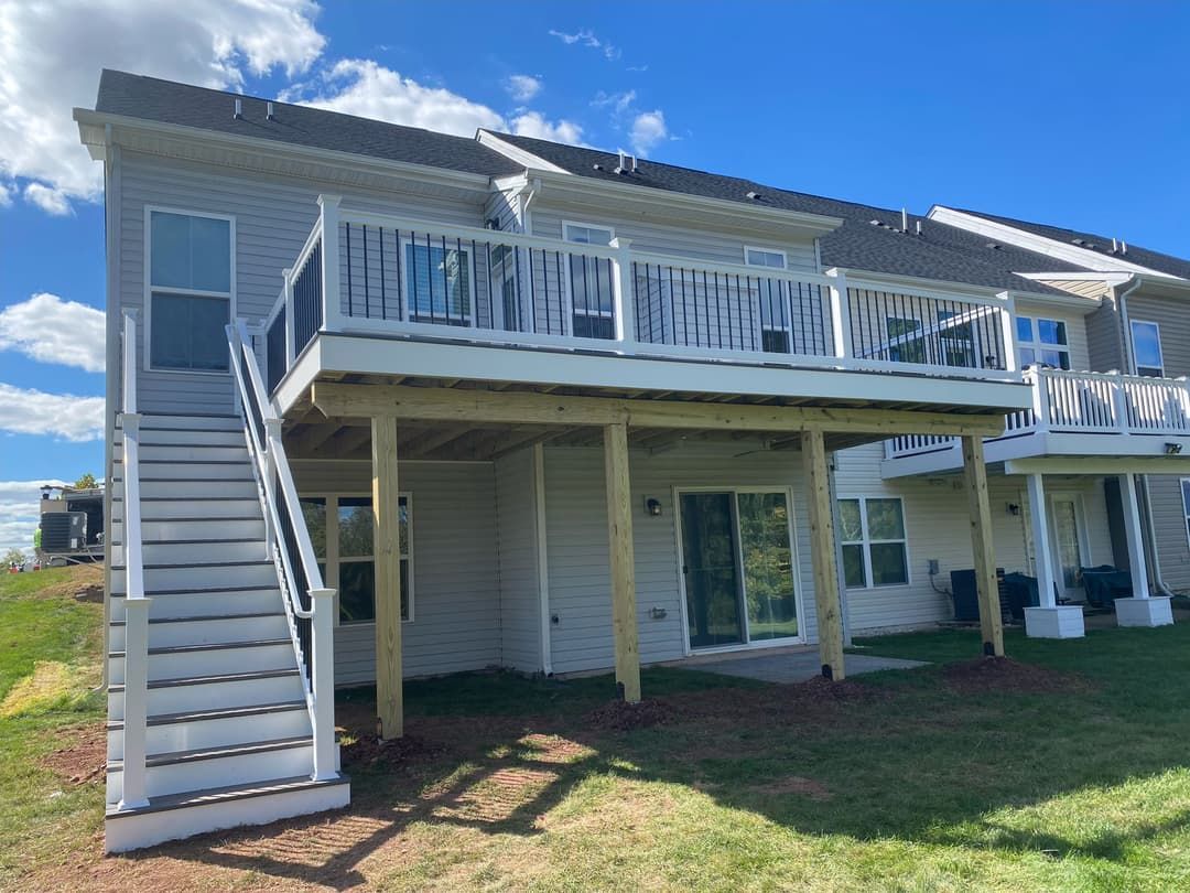 Two-story townhouse with white deck, stairs, and railing. Beige siding, blue sky, and green grass.