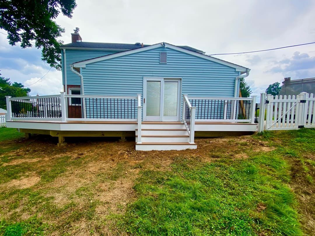 Blue house with white deck and stairs leading to sliding glass doors. White picket fence on right.