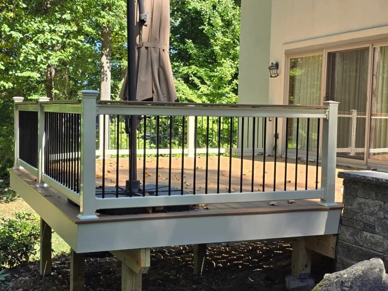 A raised wooden deck with white railing, black spindles, and a large umbrella.