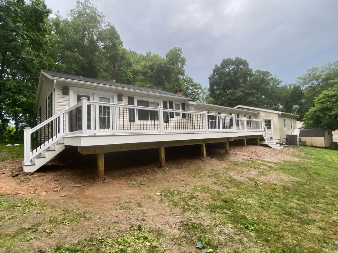 A house with a large white deck and steps, surrounded by green trees and grass.