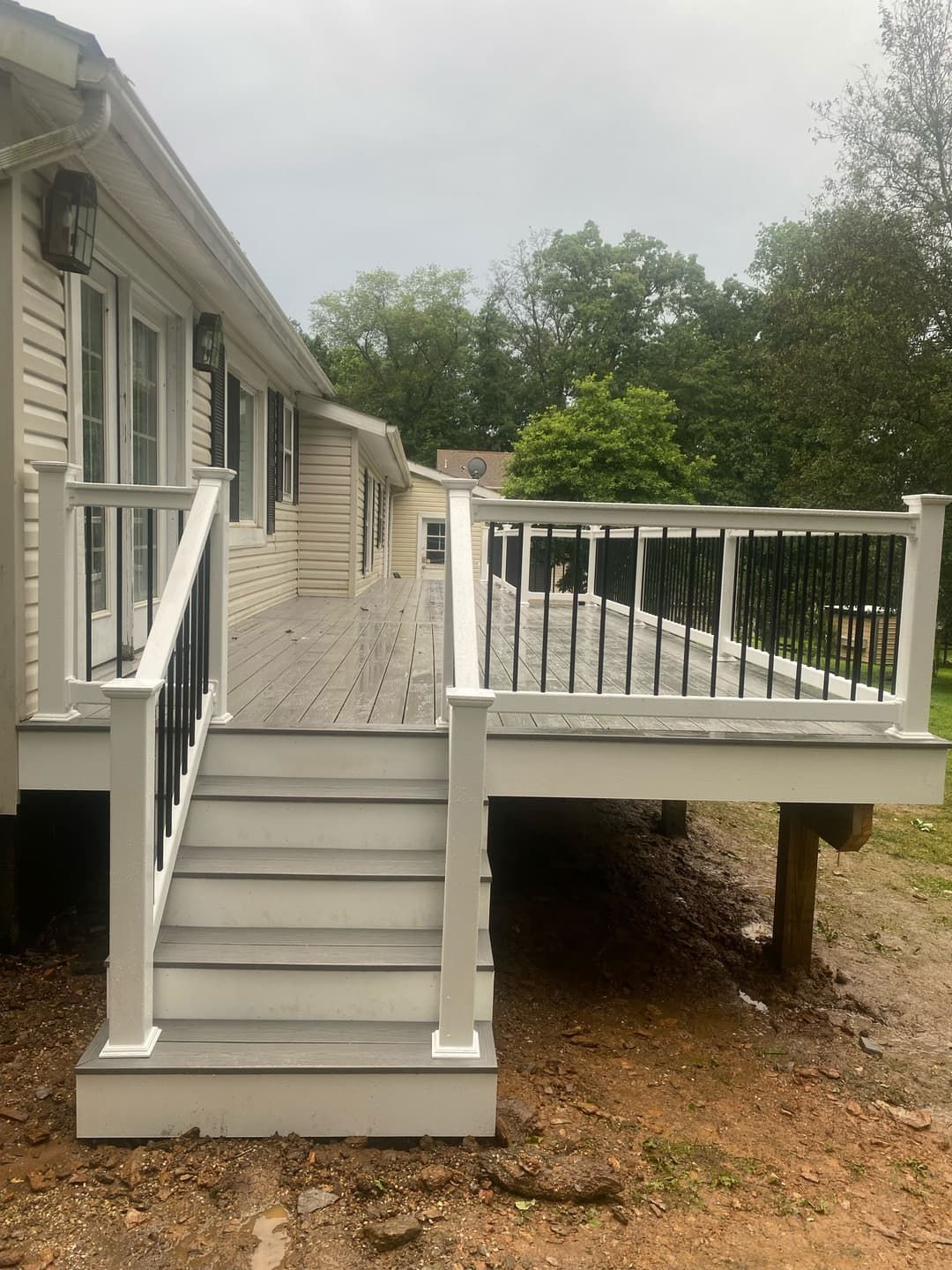 Gray deck with steps attached to a light-colored house. Black railings and white posts.