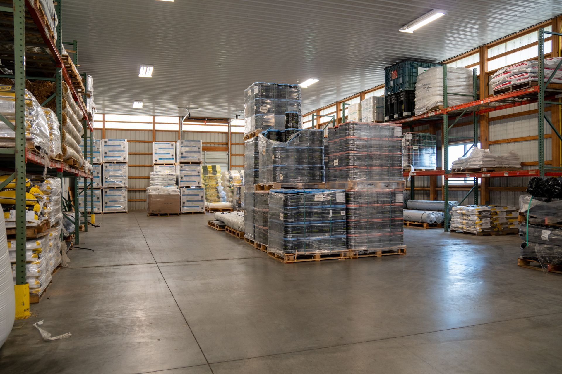 Warehouse interior with pallets of wrapped goods and shelving units.