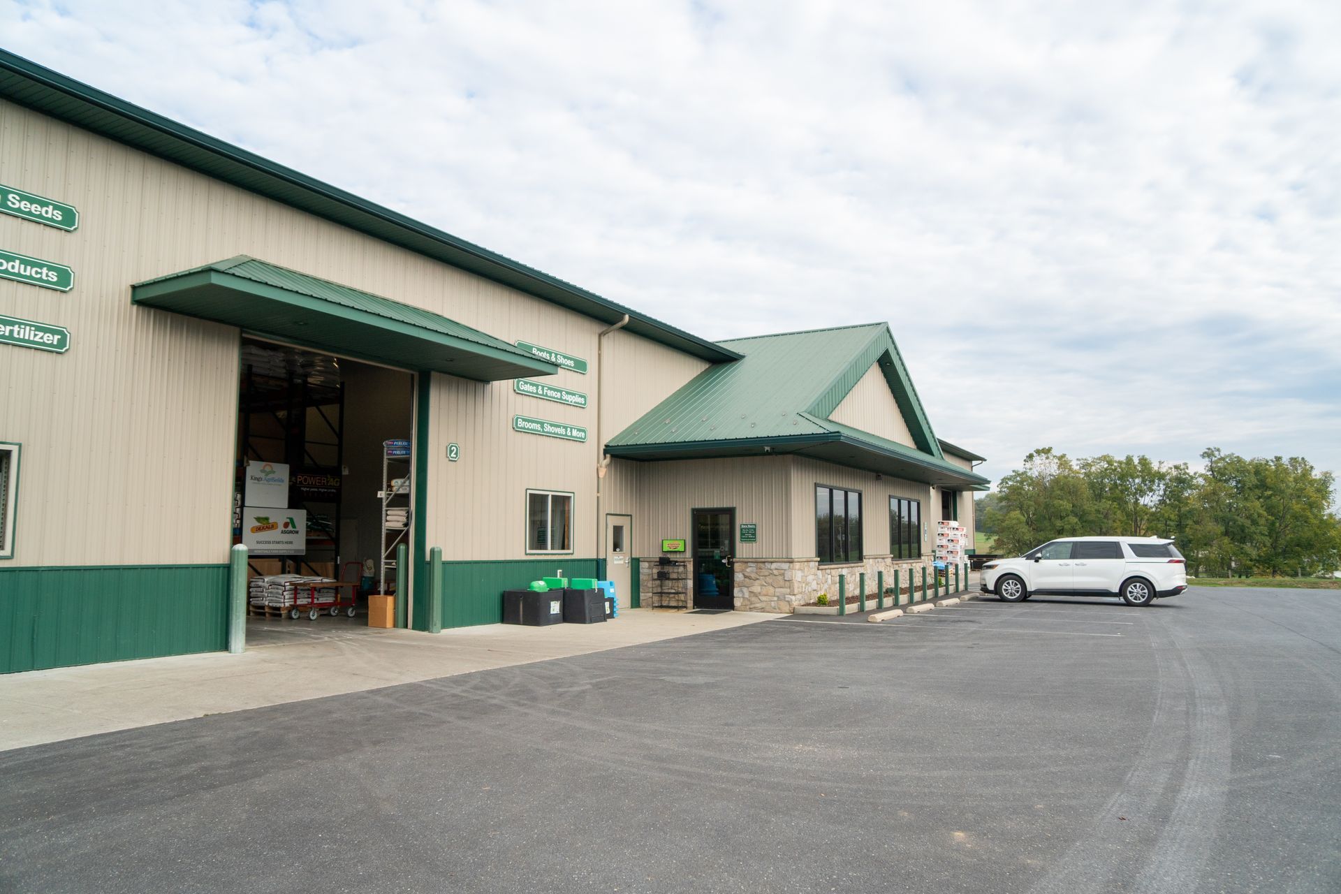 Green and beige building with open loading bay and SUV parked out front on asphalt.