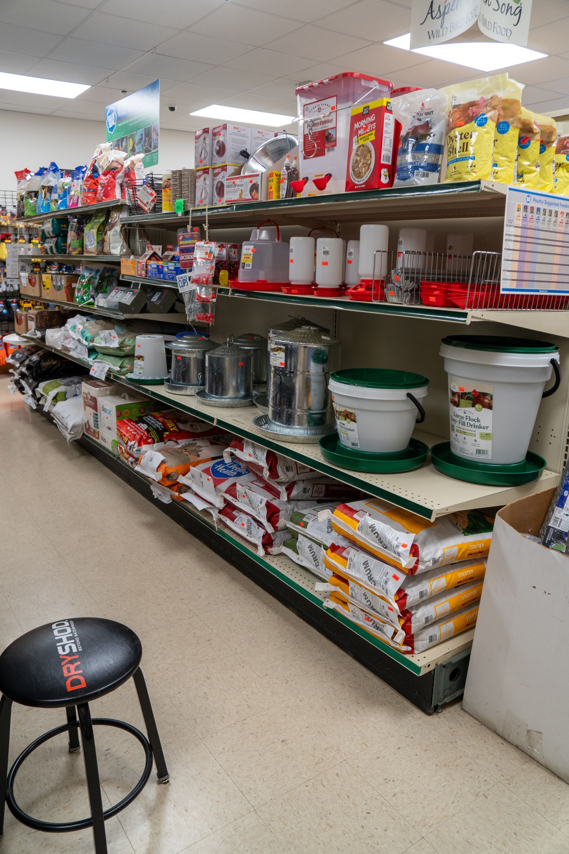 Shelves stocked with chicken feed and supplies in a store. Stool in the foreground.