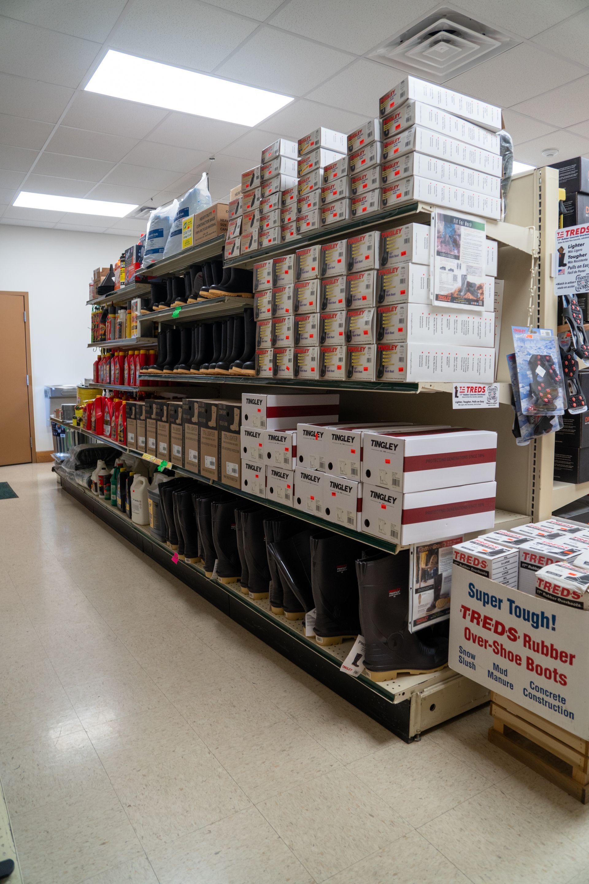 Shelves stocked with boxed boots, oil, and other merchandise in a store.