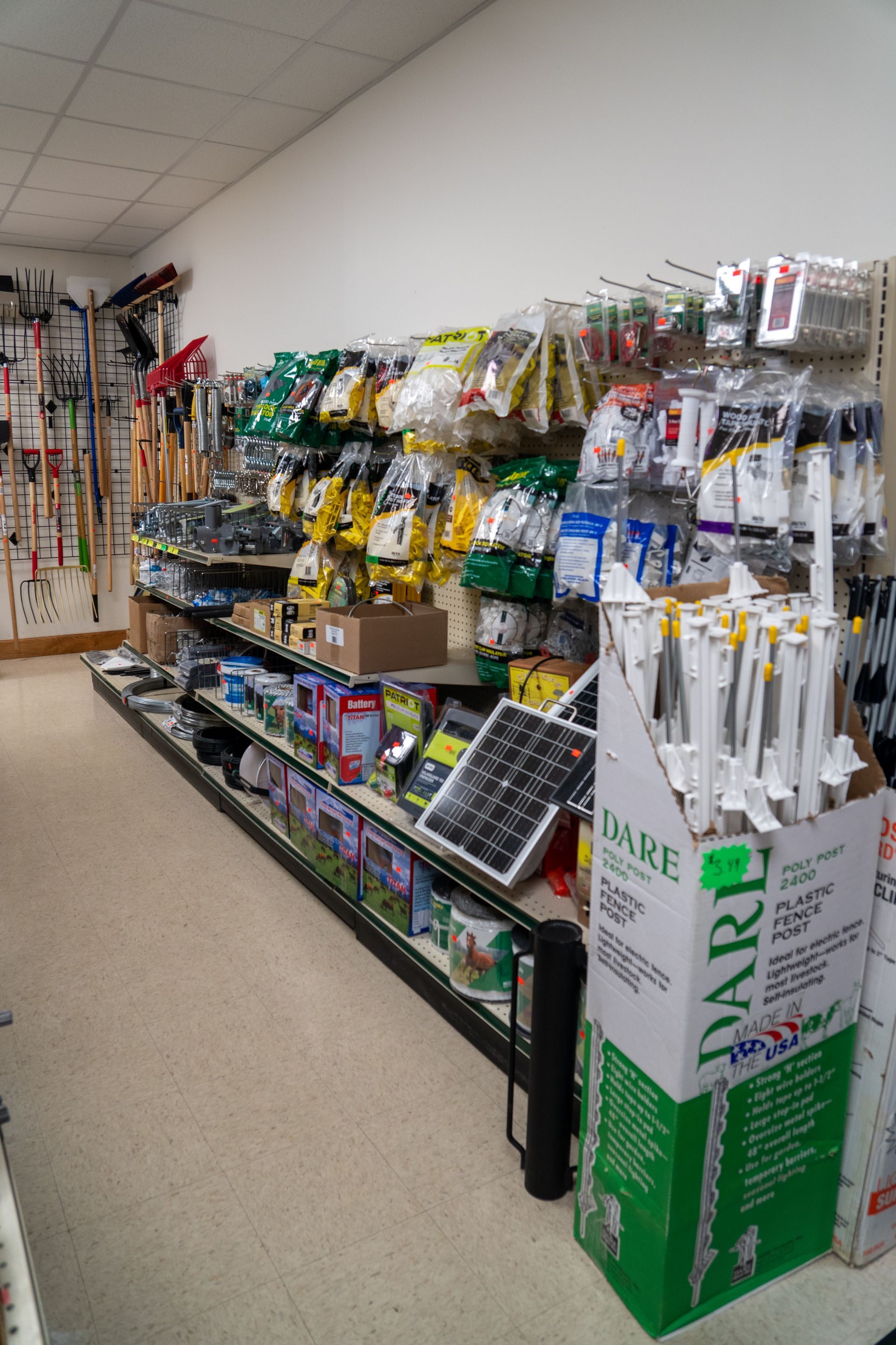 Shelves in a store filled with packaged hardware and gardening supplies. A box of white fence posts in the foreground.