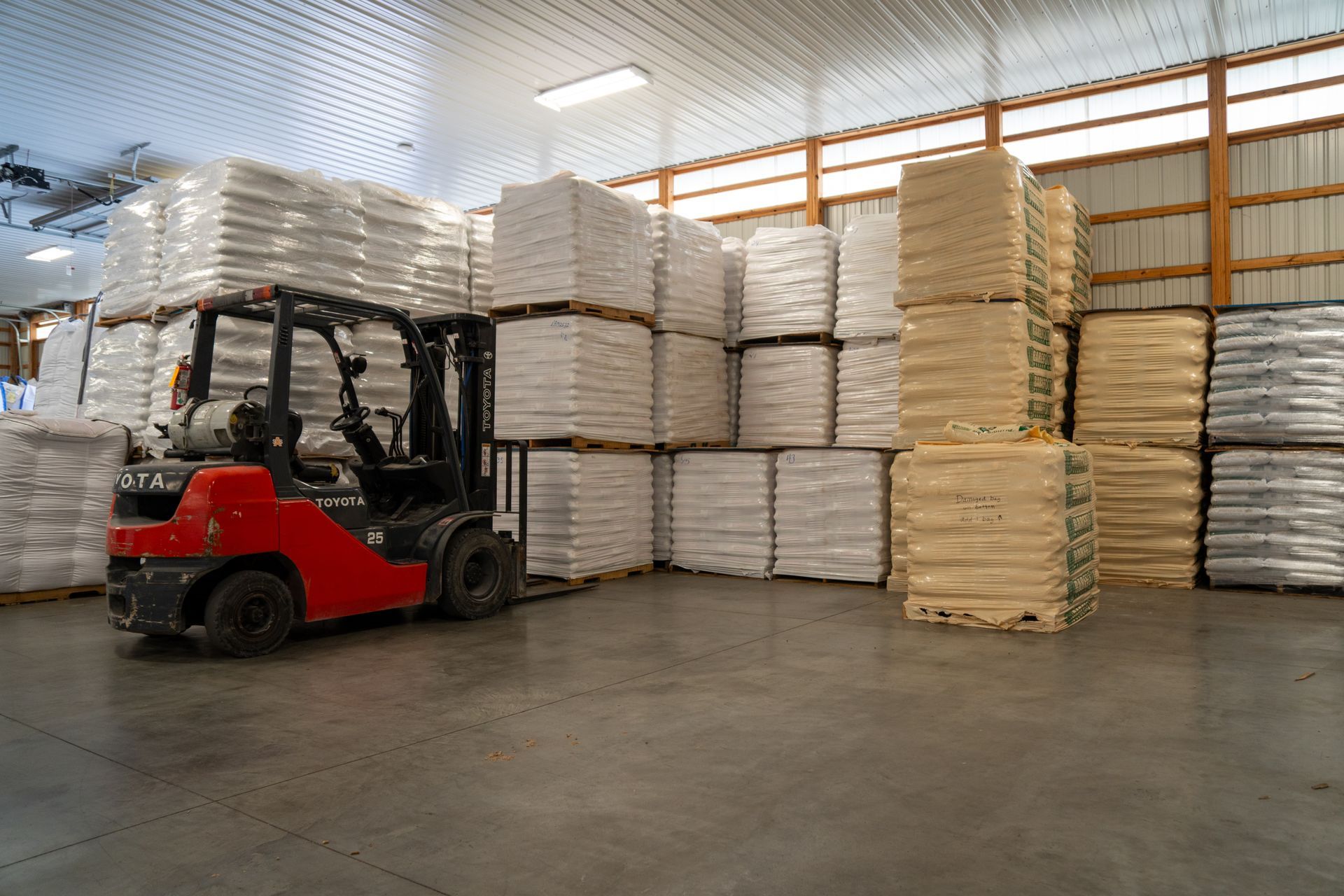Red forklift in a warehouse with pallets of bagged products.