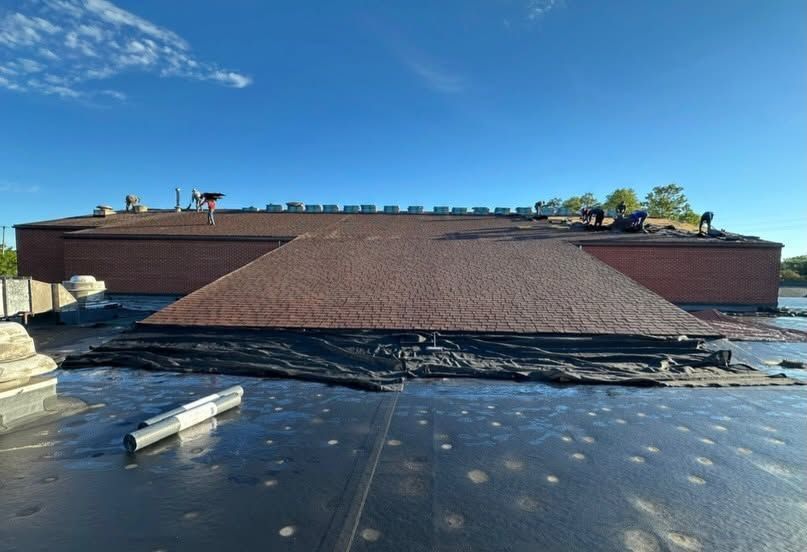 Roofing work on a low brick building under a clear blue sky