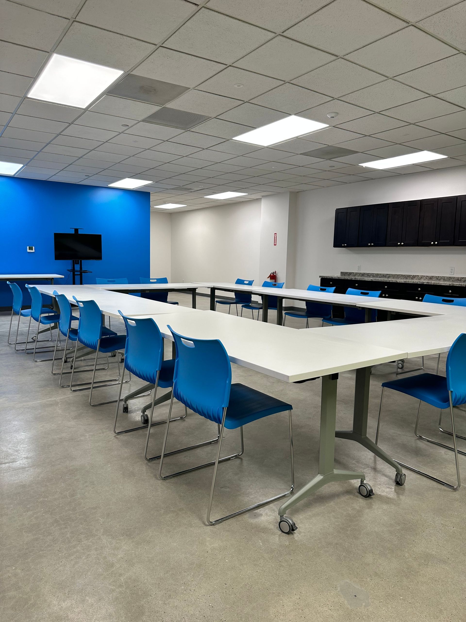 U-shaped conference table with blue chairs in a bright room with a blue accent wall and cabinets.