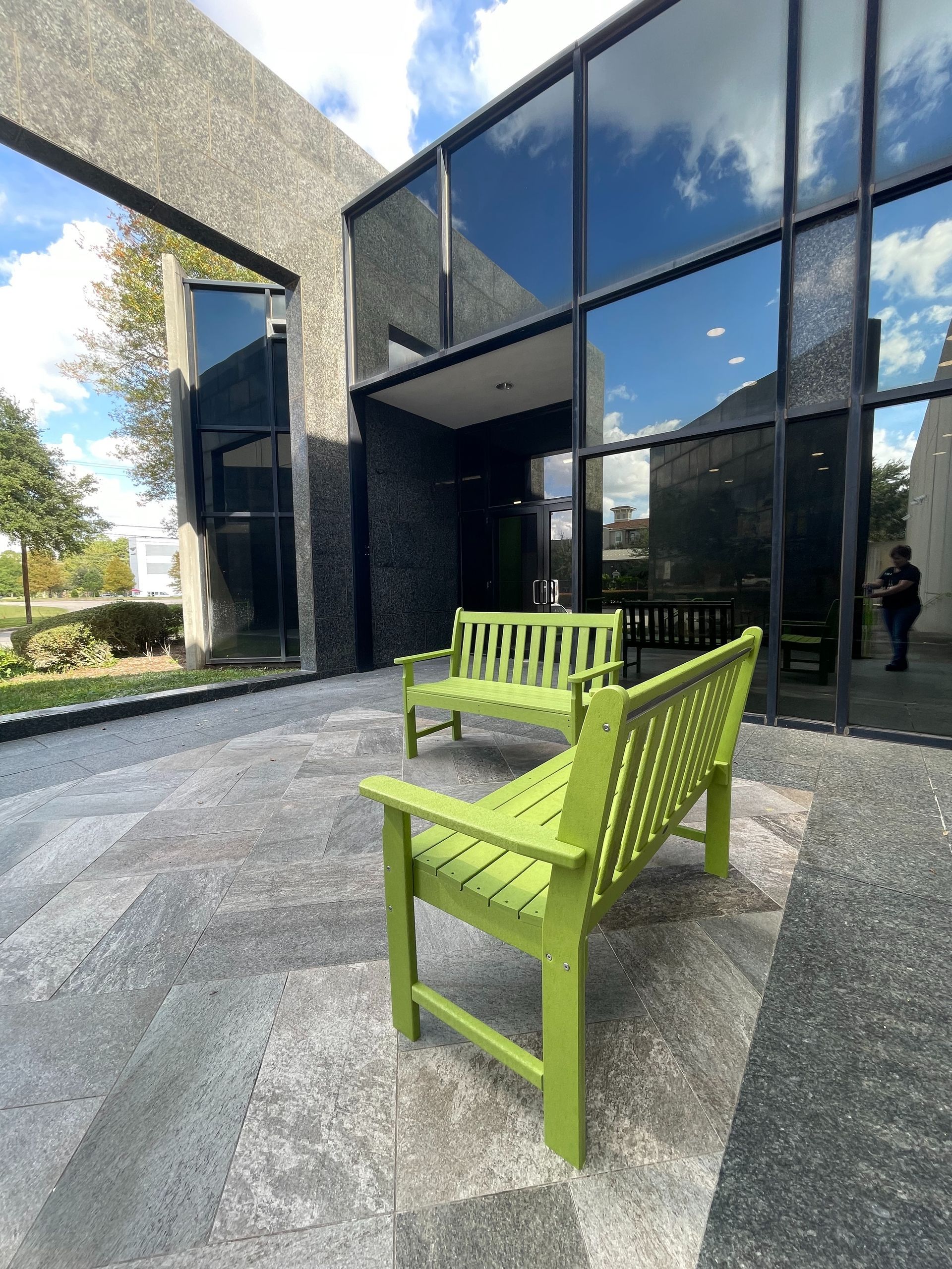 Green benches on a paved patio near a modern building with large glass windows.