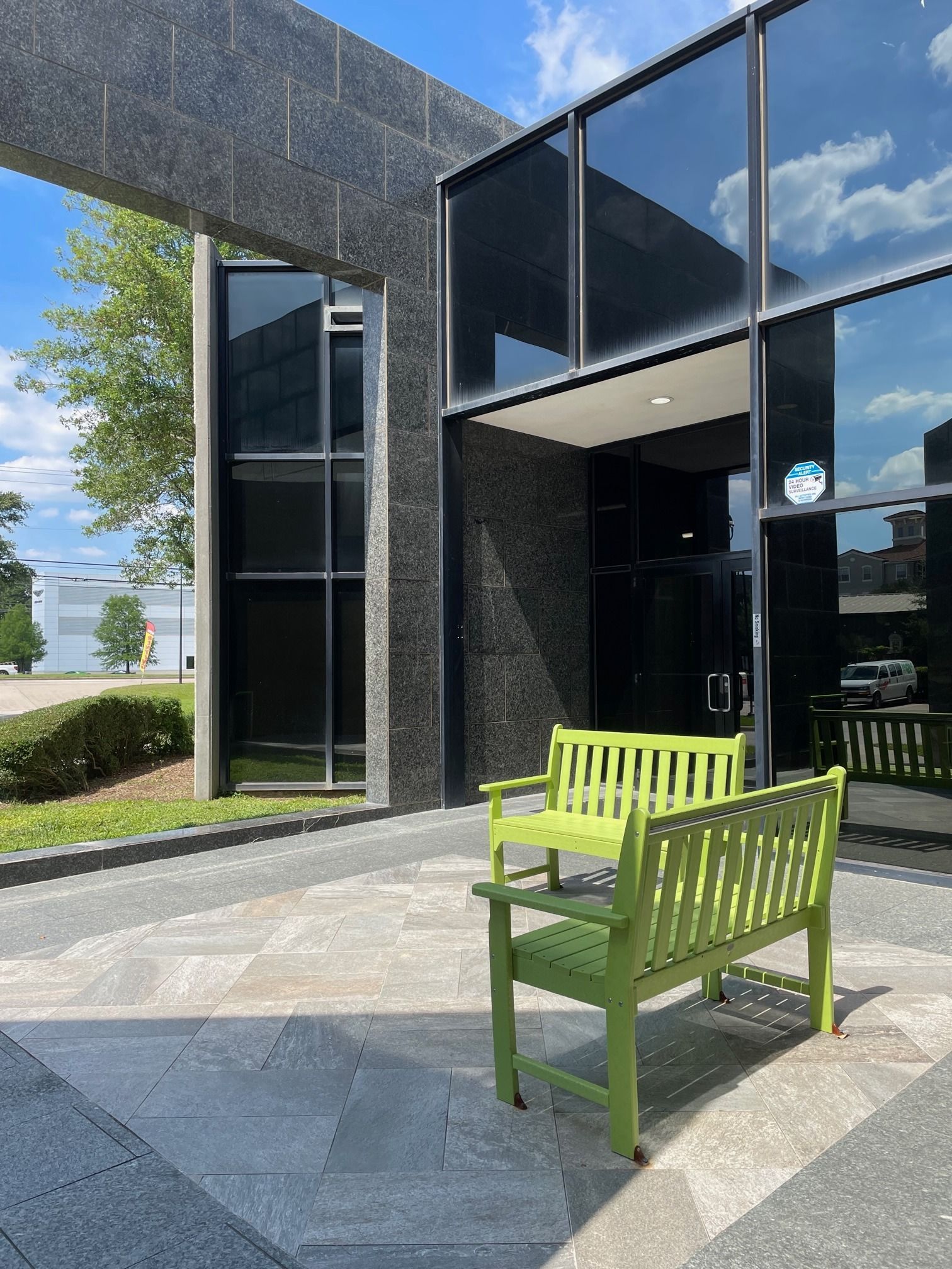 A lime green bench sits in front of a dark building with large windows reflecting the sky.