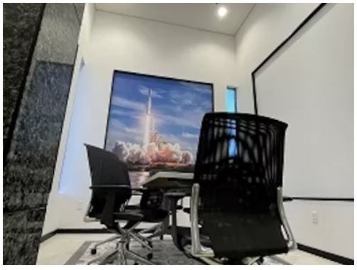 Modern office with two black chairs facing a wall-mounted rocket launch screen.
