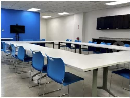 Empty conference room with U-shaped white tables, blue chairs, and wall-mounted screens