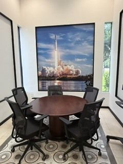 Conference room with round table, six chairs, and a large rocket launch artwork on the wall.