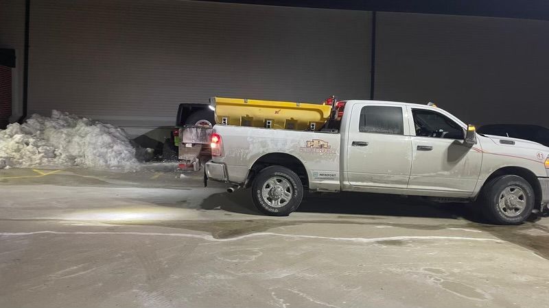 A white truck is parked in a parking lot next to a pile of snow.