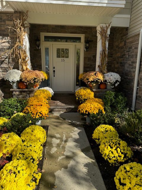 A front porch decorated with yellow and white flowers and pumpkins