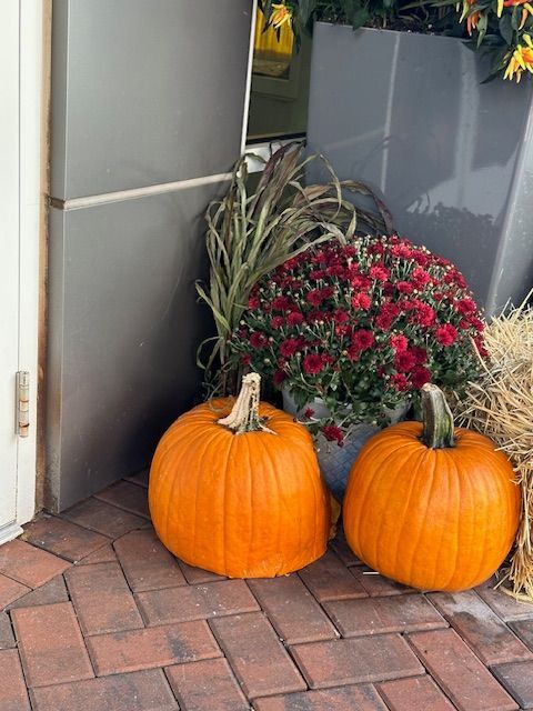 Two pumpkins are sitting on a brick sidewalk next to flowers