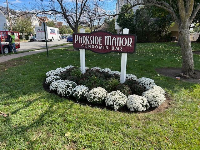 A sign for parkside manor condominiums is in the middle of a lush green field.