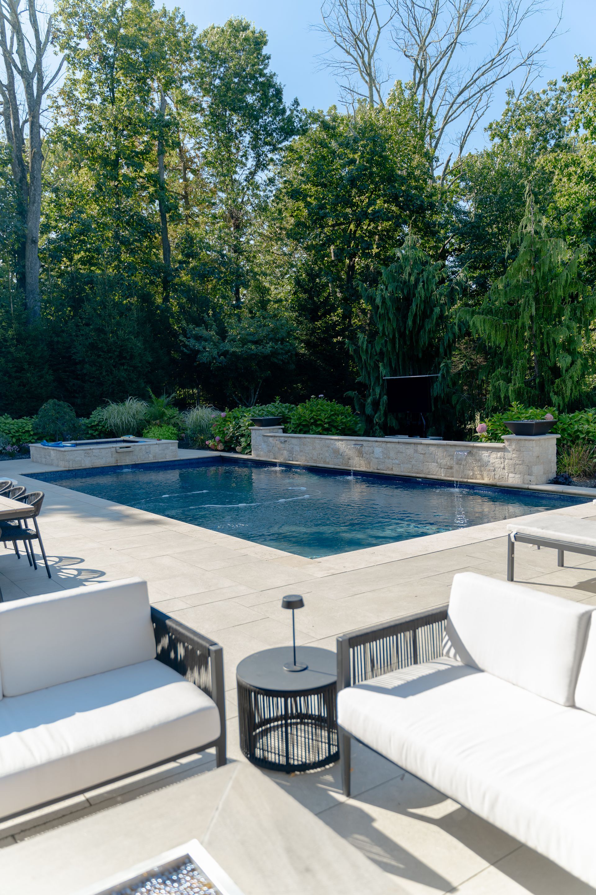 There is a large swimming pool in the backyard surrounded by trees.