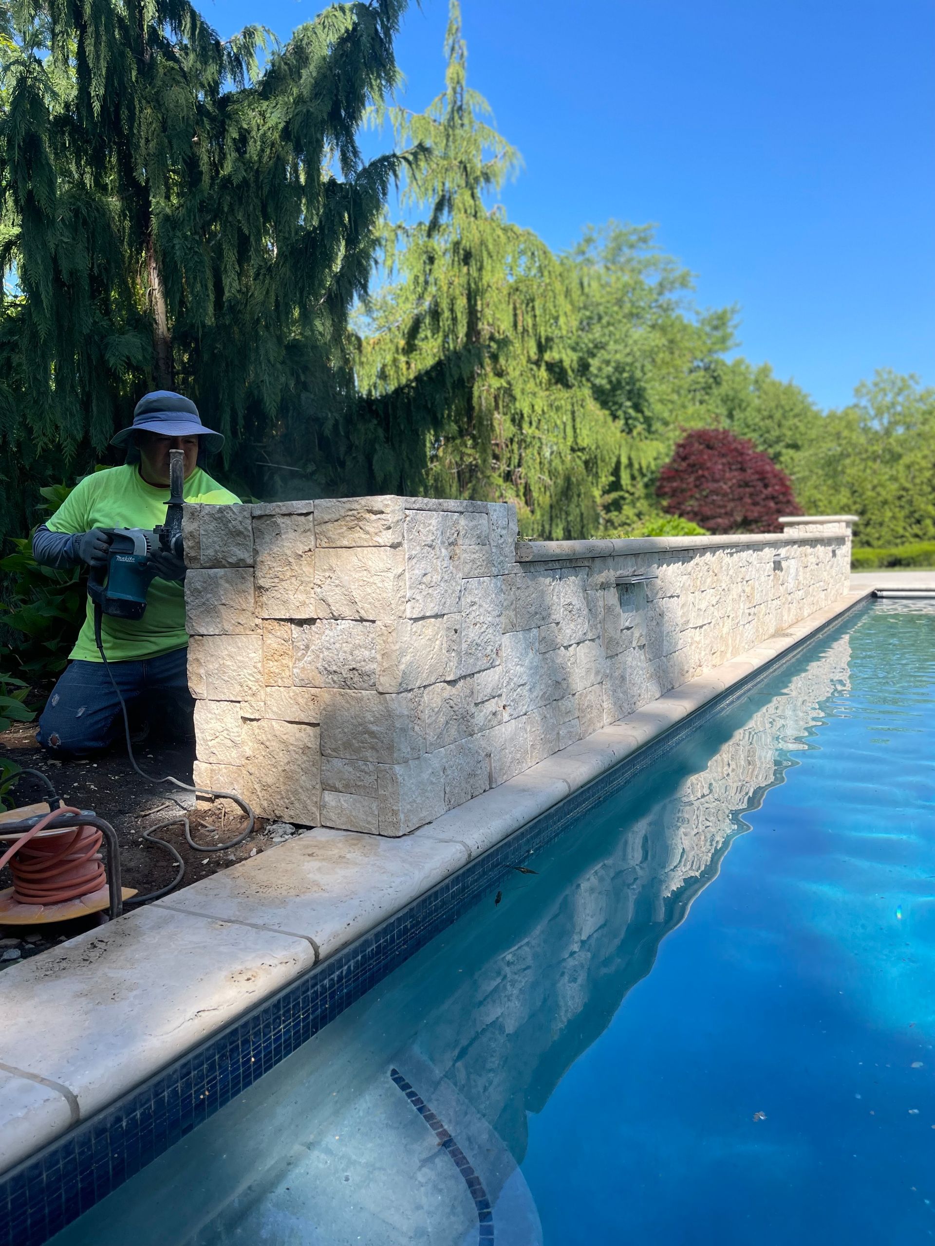 A man is working on a stone wall next to a swimming pool.