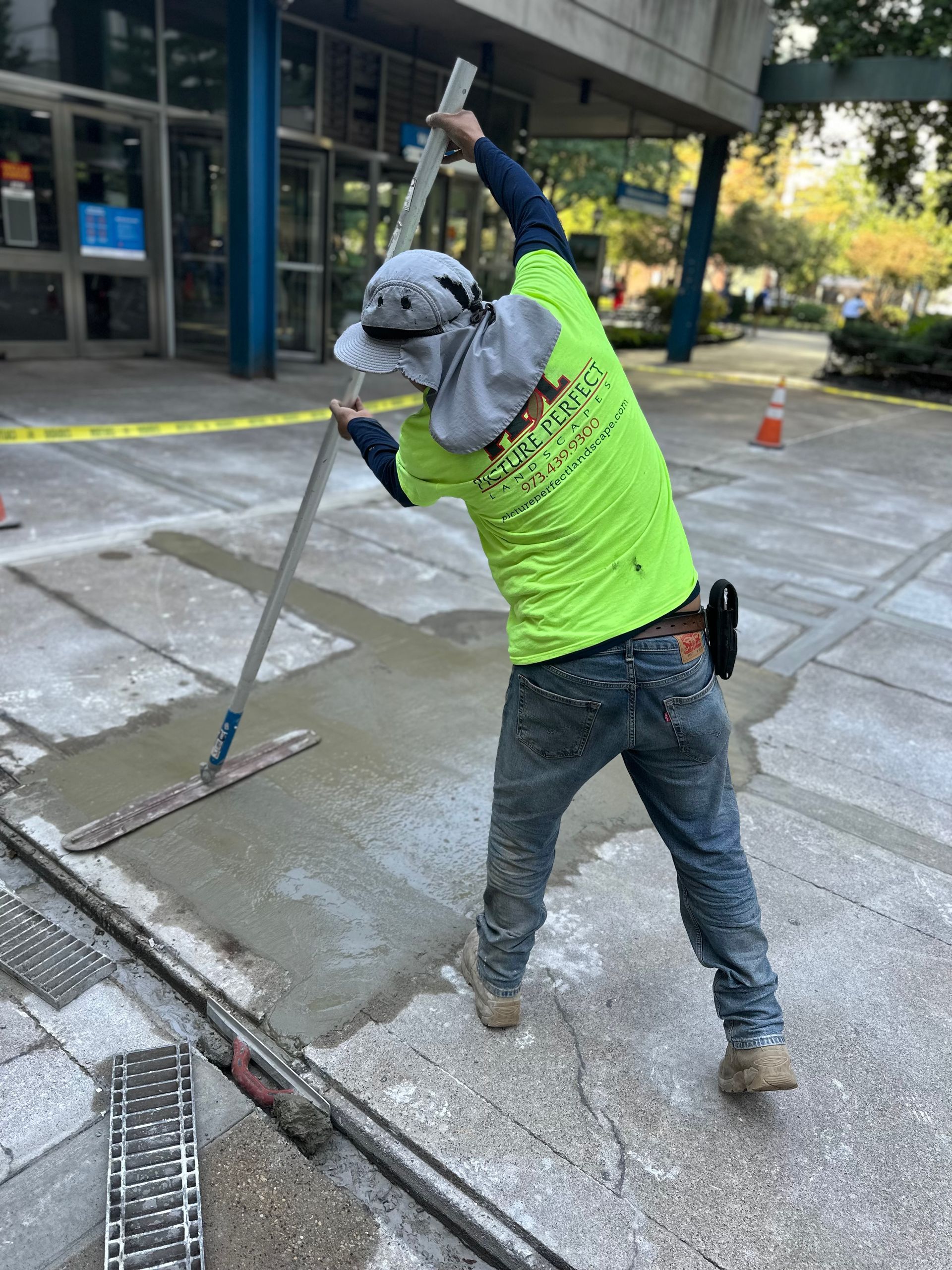 A man in a neon yellow shirt is standing on a sidewalk holding a mop.