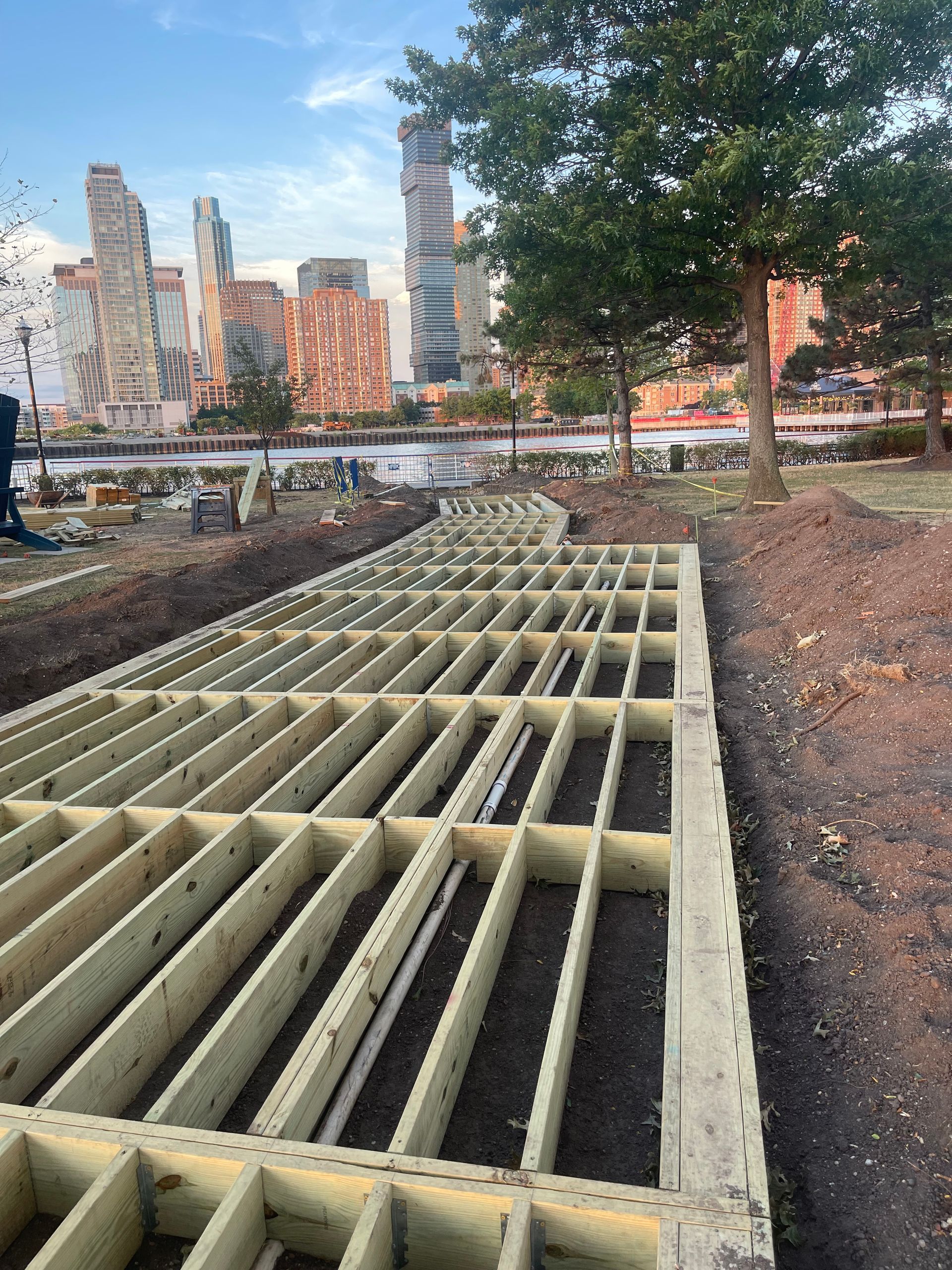 A wooden deck is being built in a park with a city skyline in the background.