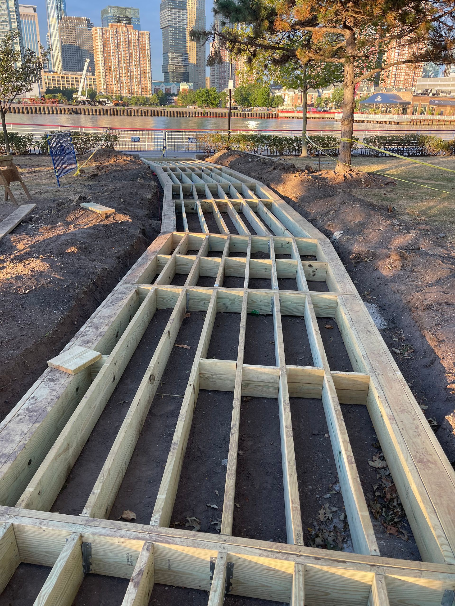 A wooden walkway is being built in a park with a city in the background.