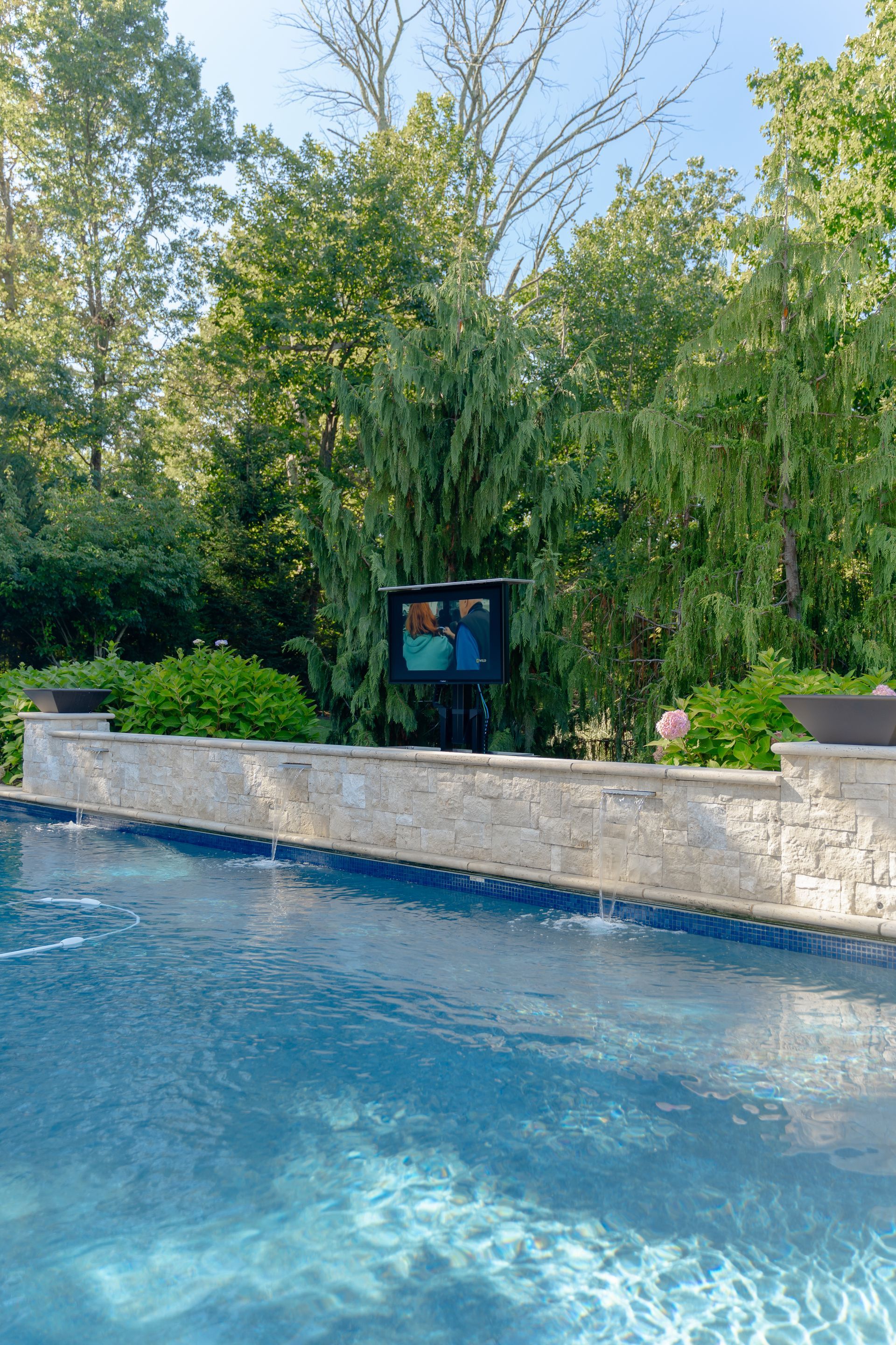 A large swimming pool surrounded by trees and a stone wall.