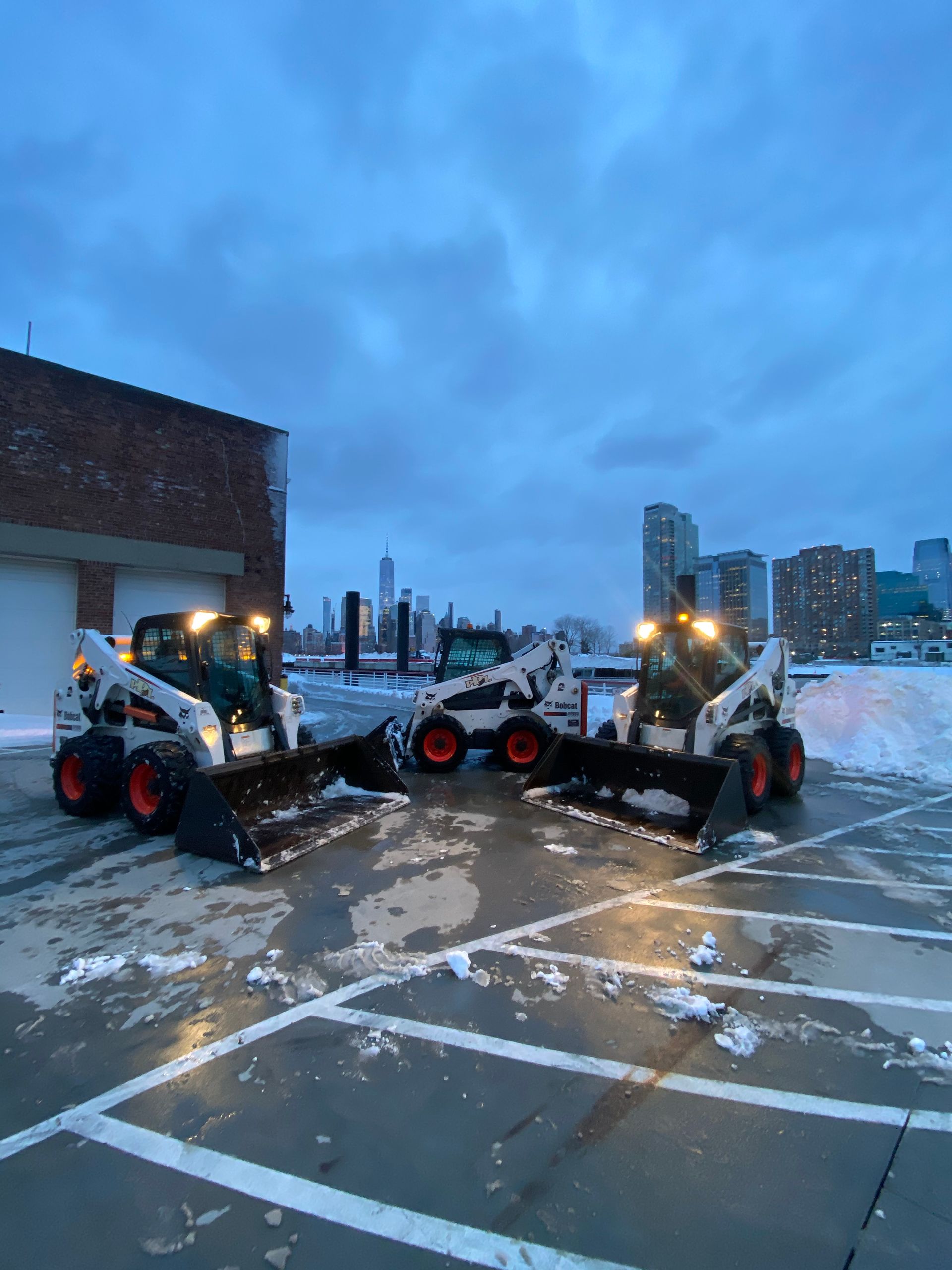 Three snow plows are parked in a parking lot.
