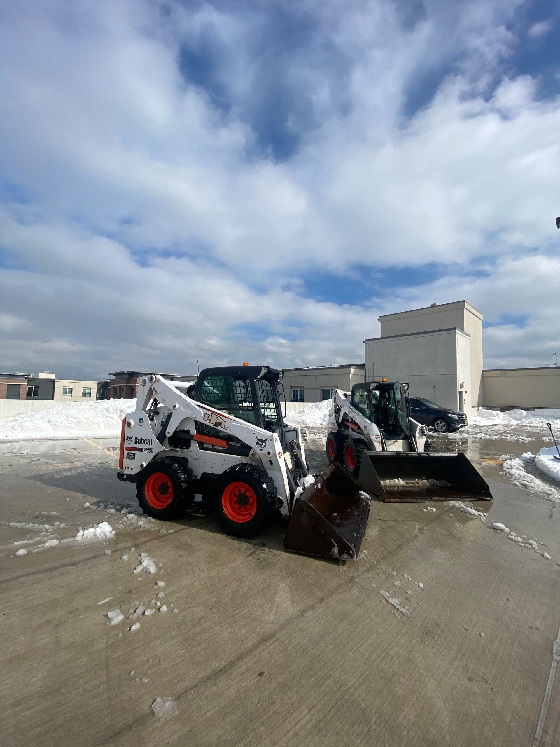 Two bobcat loaders are parked next to each other in a parking lot.