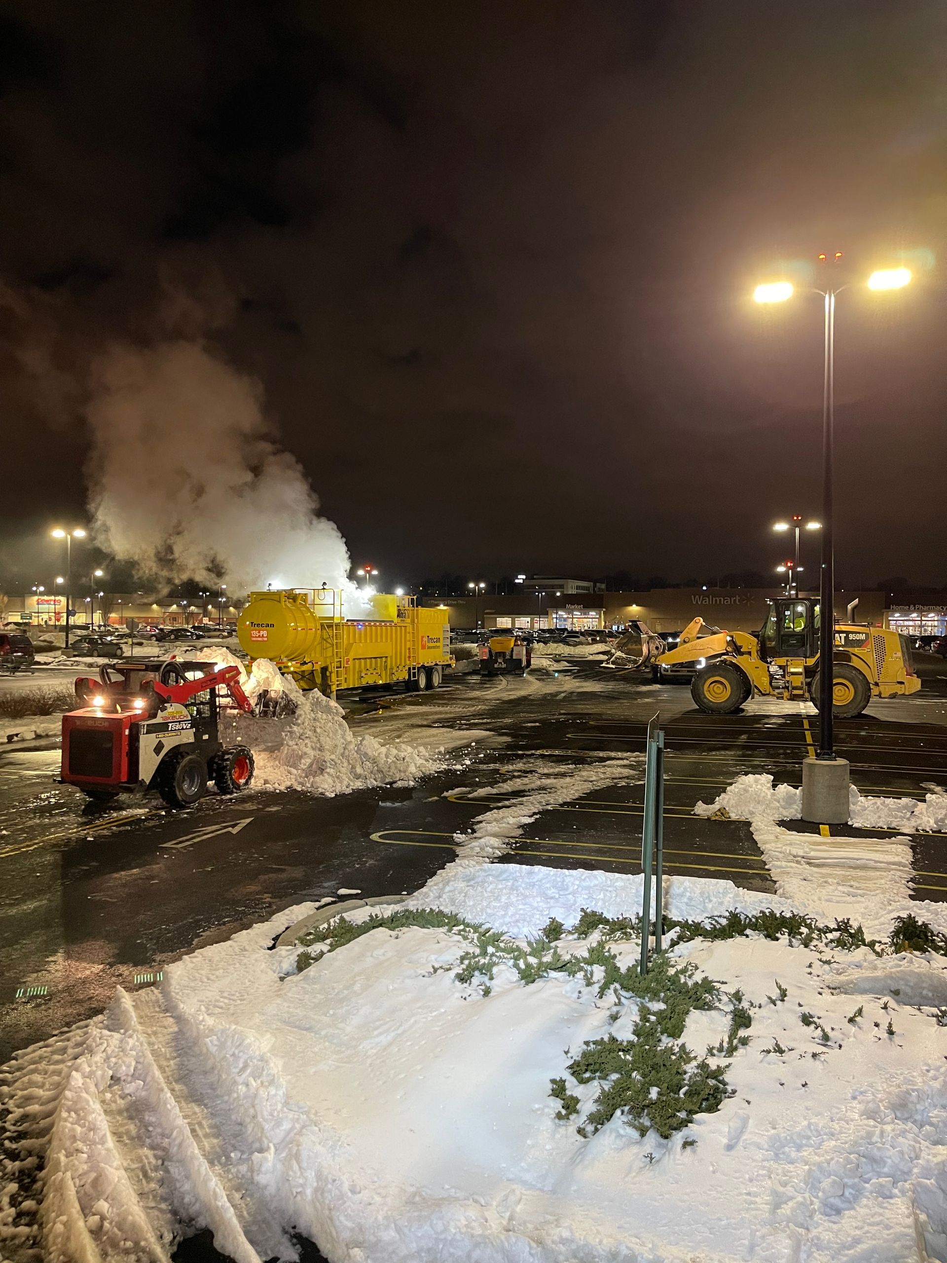 A lot of snow plows are in a parking lot at night.