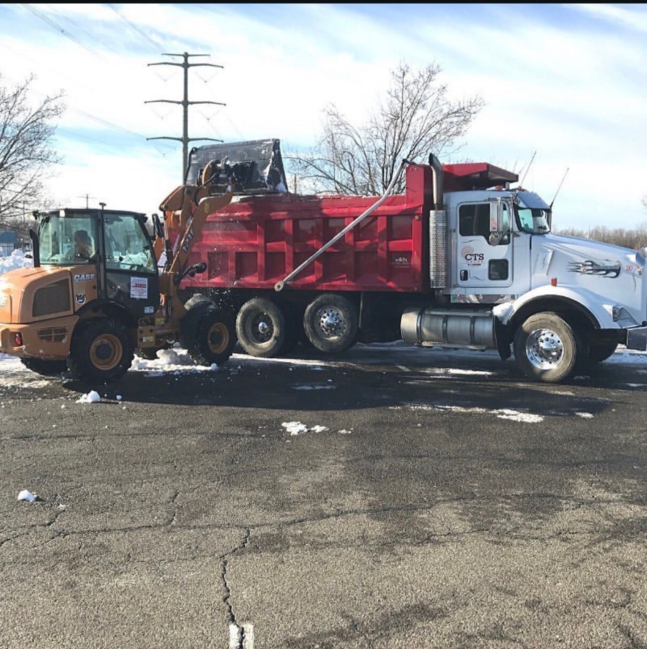 A dump truck is parked next to a tractor in a parking lot