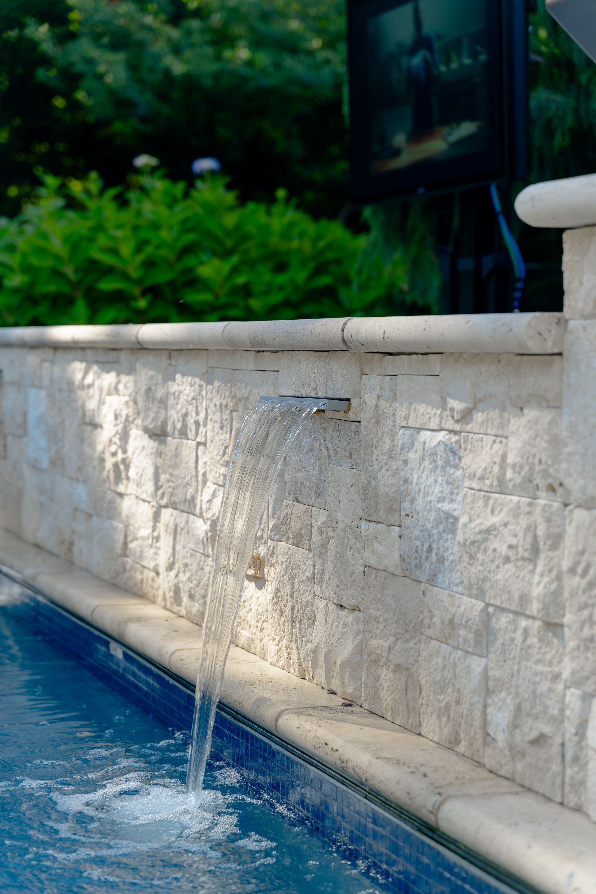 A waterfall is coming out of the side of a swimming pool.