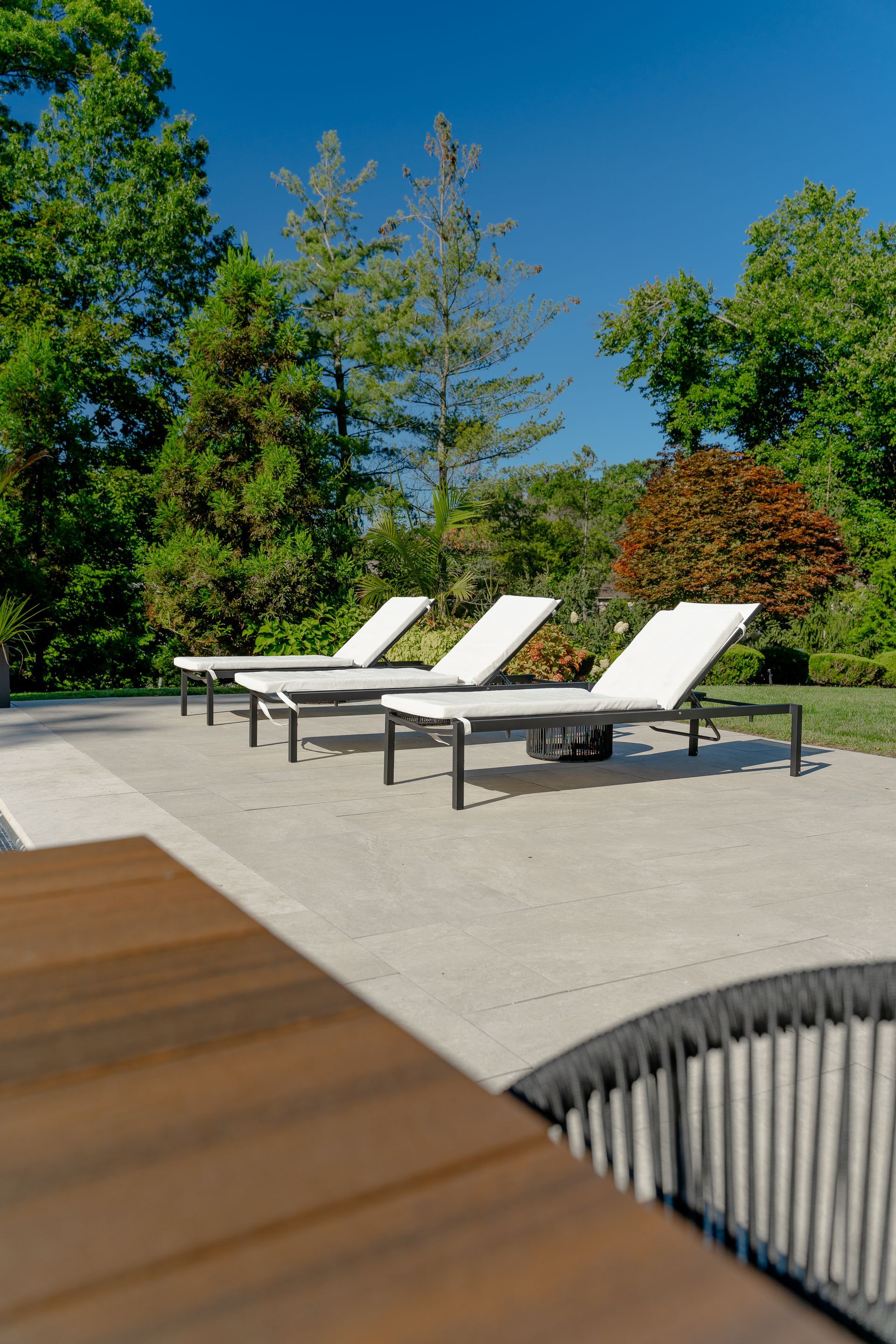 A row of lounge chairs are sitting on a patio next to a table.